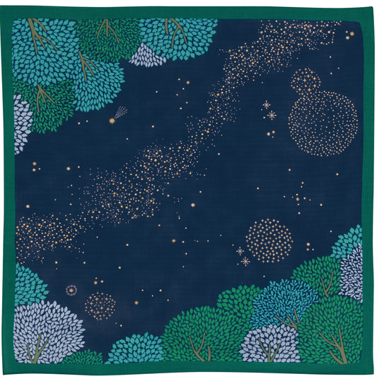Flat lay view of a navy blue Japanese furoshiki cloth featuring an illustrated night sky pattern with a starry milky way and a border of green forest trees.
