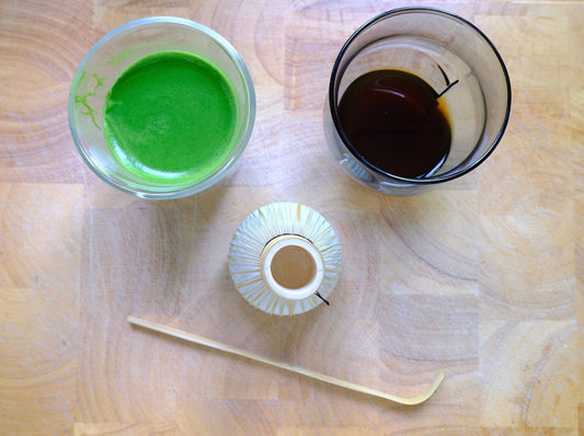 Flat lay view of whisked green matcha, black coffee, a bamboo whisk (chasen), and a bamboo scoop on a wooden board at a local Tea Studio Lu, the best matcha online shop in Switzerland, Geneva. Specialty tea shop.