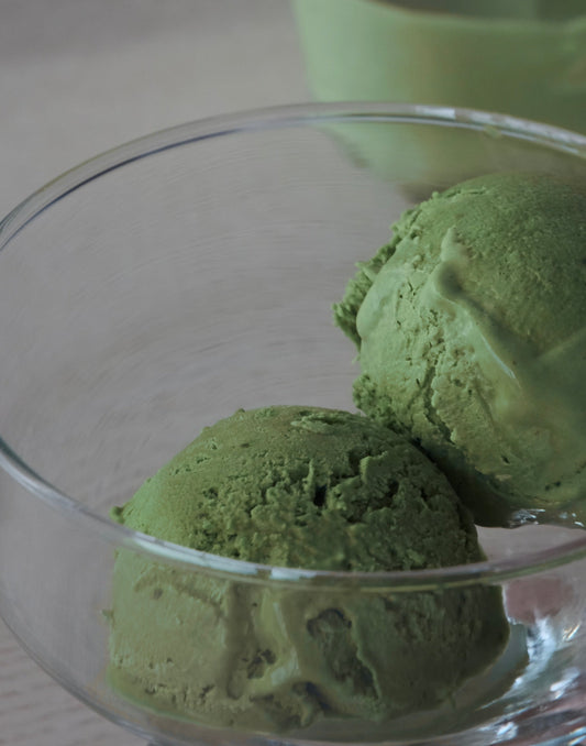 Matcha green tea icTwo perfect scoops of vibrant green matcha ice cream served in a minimalist glass bowl, highlighting the premium matcha available at Tea Studio Lu in Switzerland