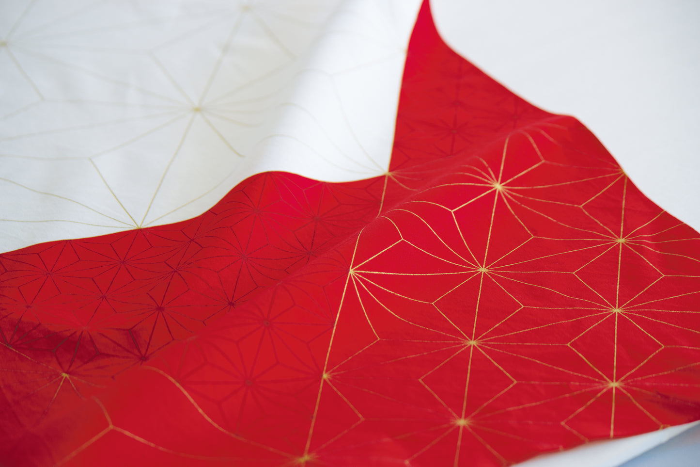 Close-up texture shot of a red and white Japanese furoshiki cloth featuring elegant gold geometric Asanha hemp leaf star patterns on wavy folds.