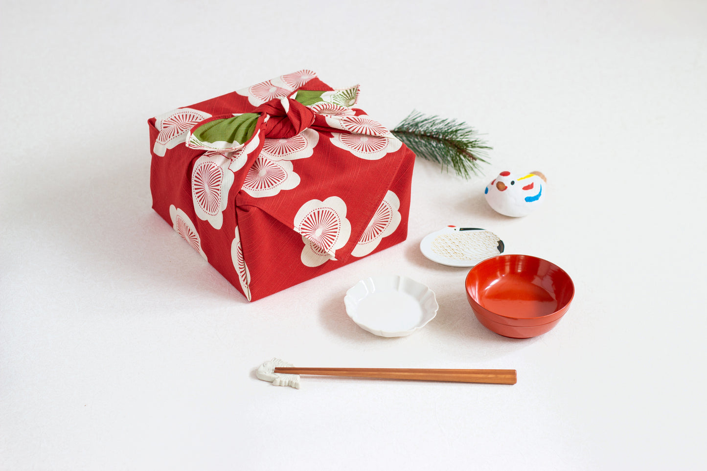 Eco-friendly gift wrapping using a red and green reversible apricot blossom furoshiki cloth on a square box, styled on a white surface with traditional Japanese tableware and chopsticks
