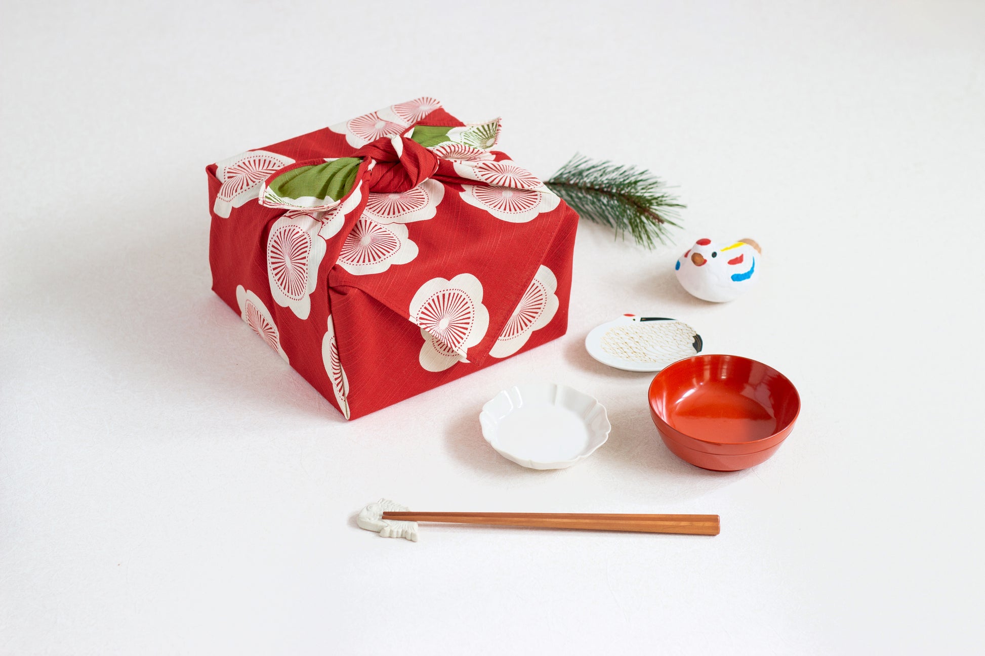 Eco-friendly gift wrapping using a red and green reversible apricot blossom furoshiki cloth on a square box, styled on a white surface with traditional Japanese tableware and chopsticks