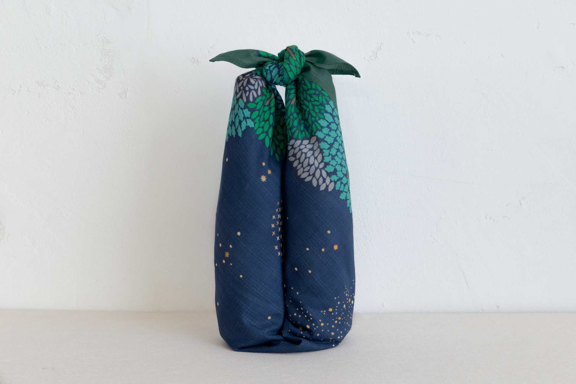 Two bottle of sake or wine neatly wrapped in a navy blue and forest green starry night furoshiki cloth with a secure top knot, isolated against a plain white background.