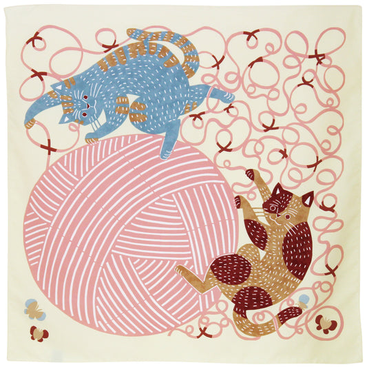 Flat lay view of a square Japanese furoshiki cloth showing a playful illustration of a blue cat and a brown cat playing with a large pink ball of yarn.