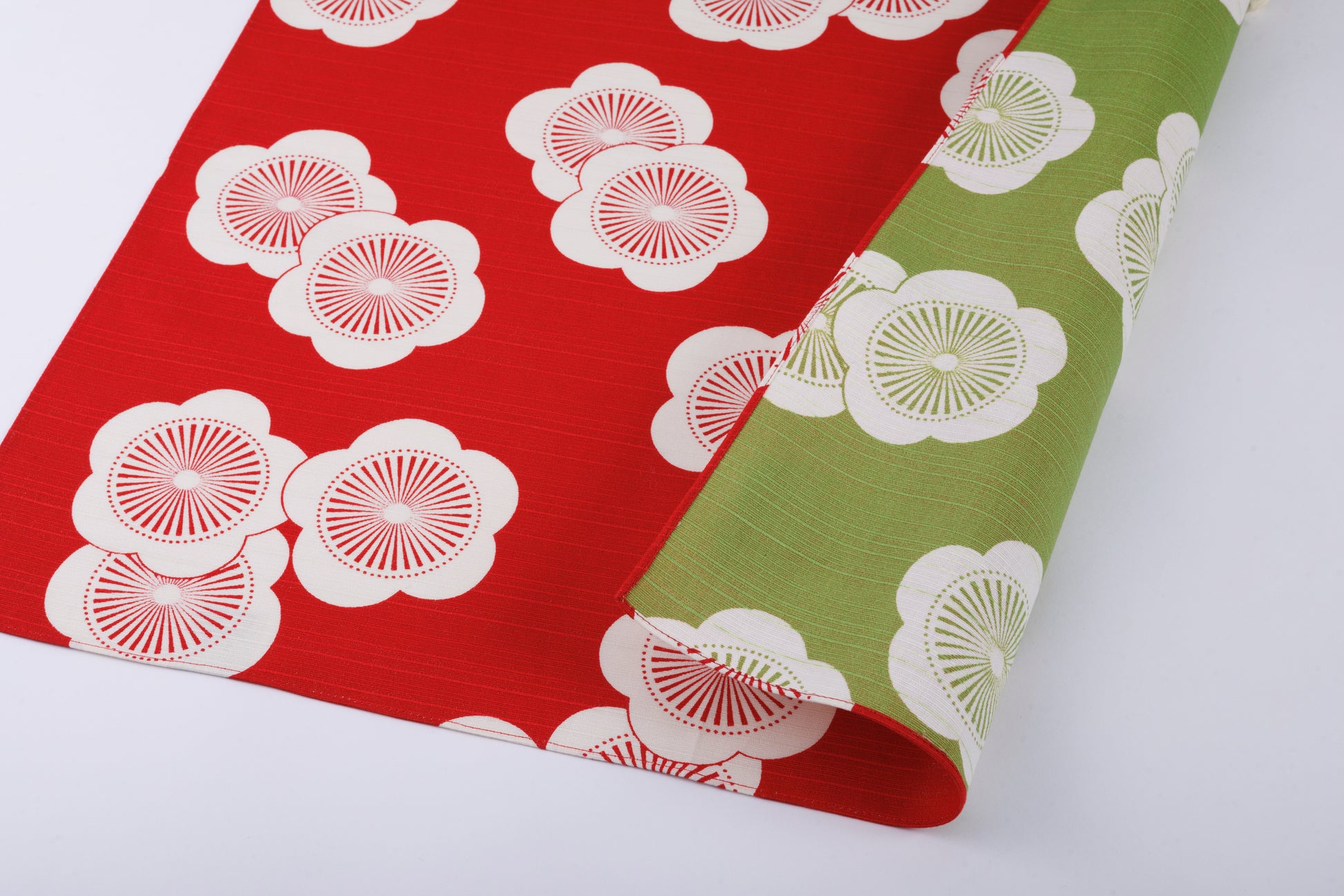 Flat lay view of a reversible Japanese furoshiki wrapping cloth, showcasing a dual-sided design with white apricot blossom patterns on a red background and a contrasting olive green side.