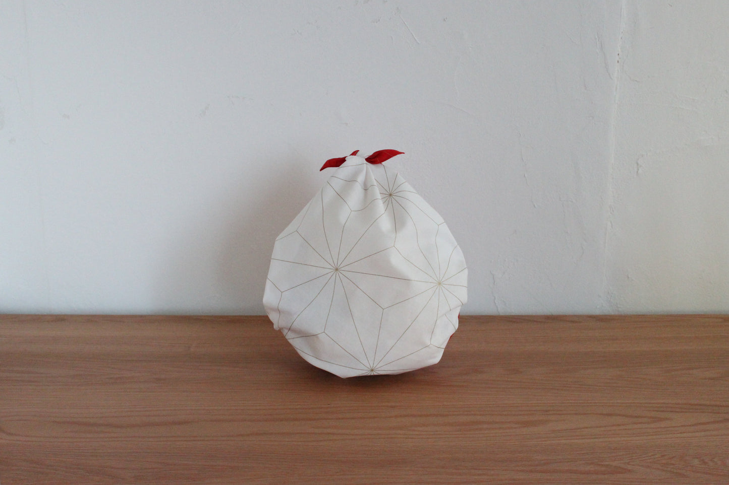 Reusable Japanese furoshiki bag tied into a drop-style pouch on a wooden tabletop, showcasing the white side of a reversible cloth decorated with fine gold star line work.