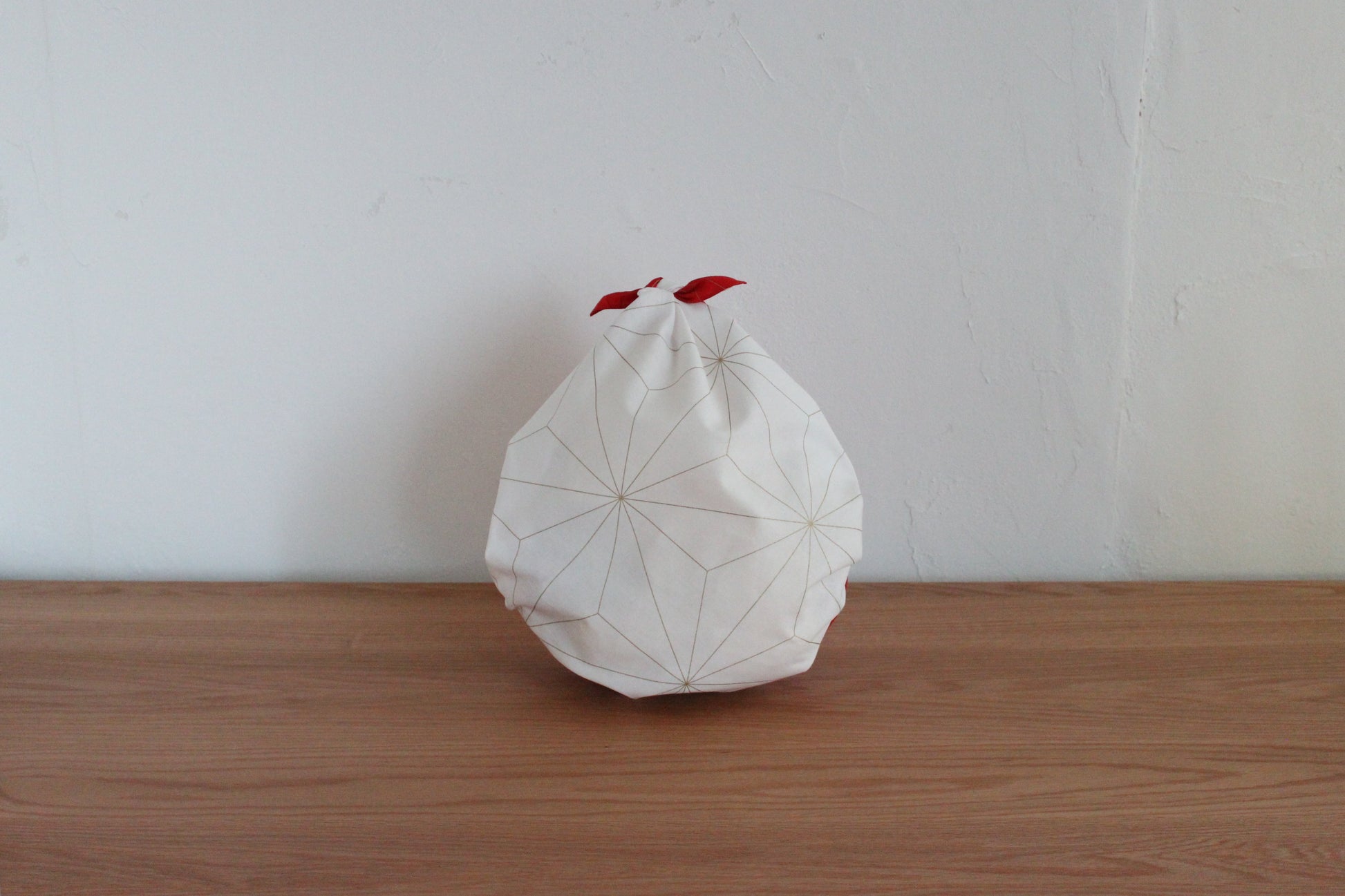 Reusable Japanese furoshiki bag tied into a drop-style pouch on a wooden tabletop, showcasing the white side of a reversible cloth decorated with fine gold star line work.