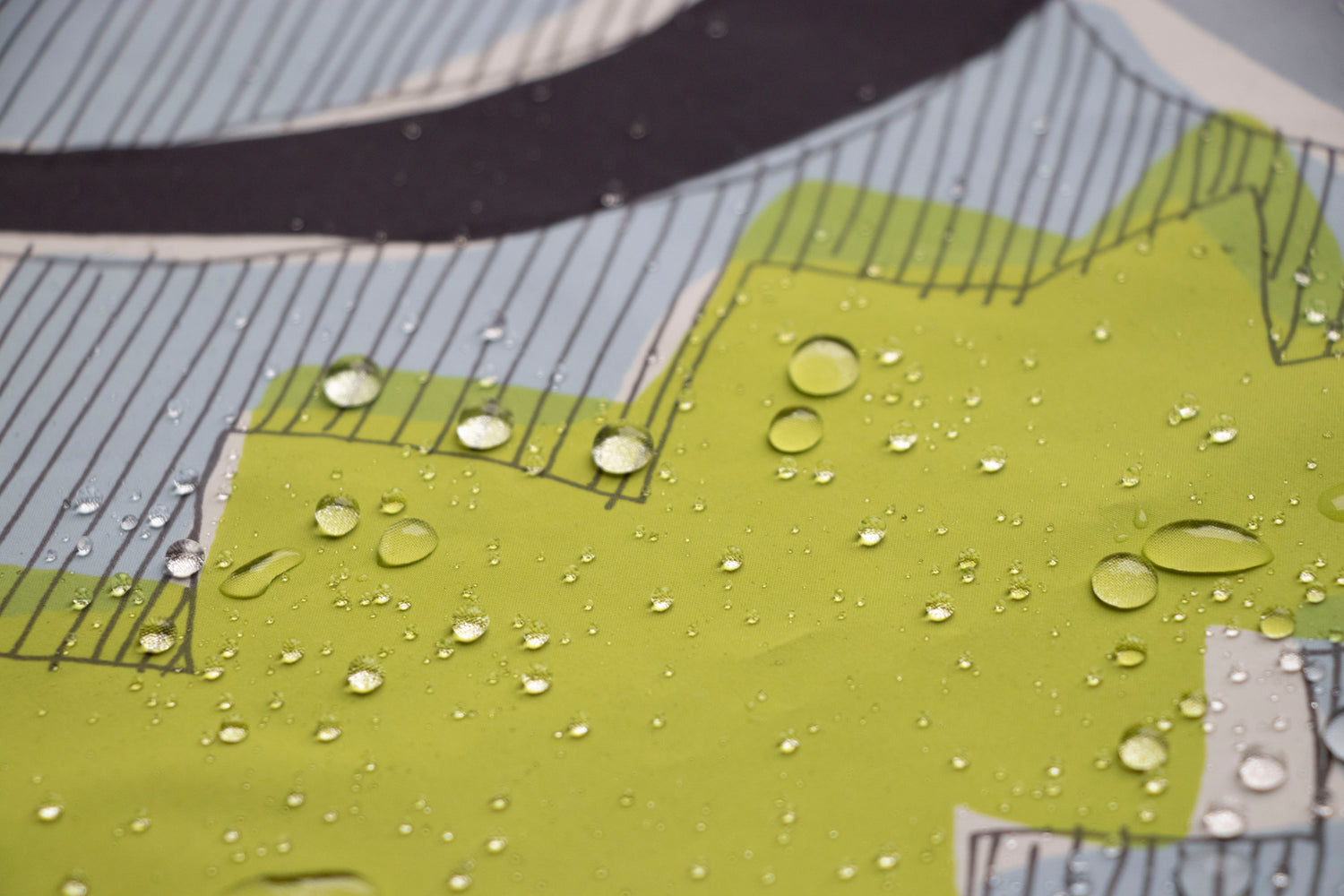 A detailed close-up showing water droplets sitting on a water-resistant fabric. The fabric features a modern illustration with bright green shapes, fine vertical black lines, and a light blue background.