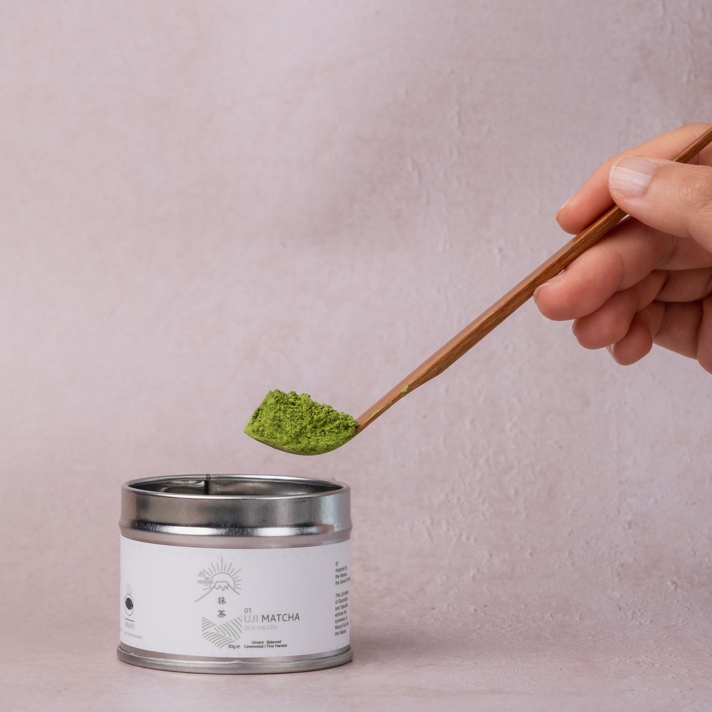 Hand scooping vibrant green ceremonial matcha powder from a canister using a wooden spoon