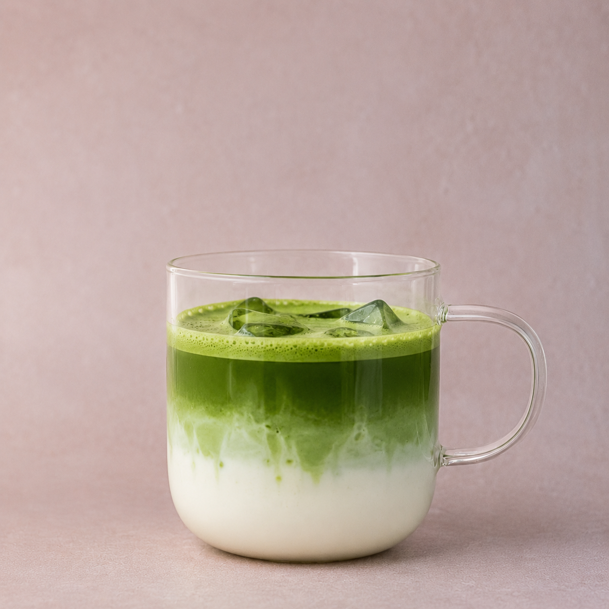 Clear glass mug with layered matcha latte on a light pink background