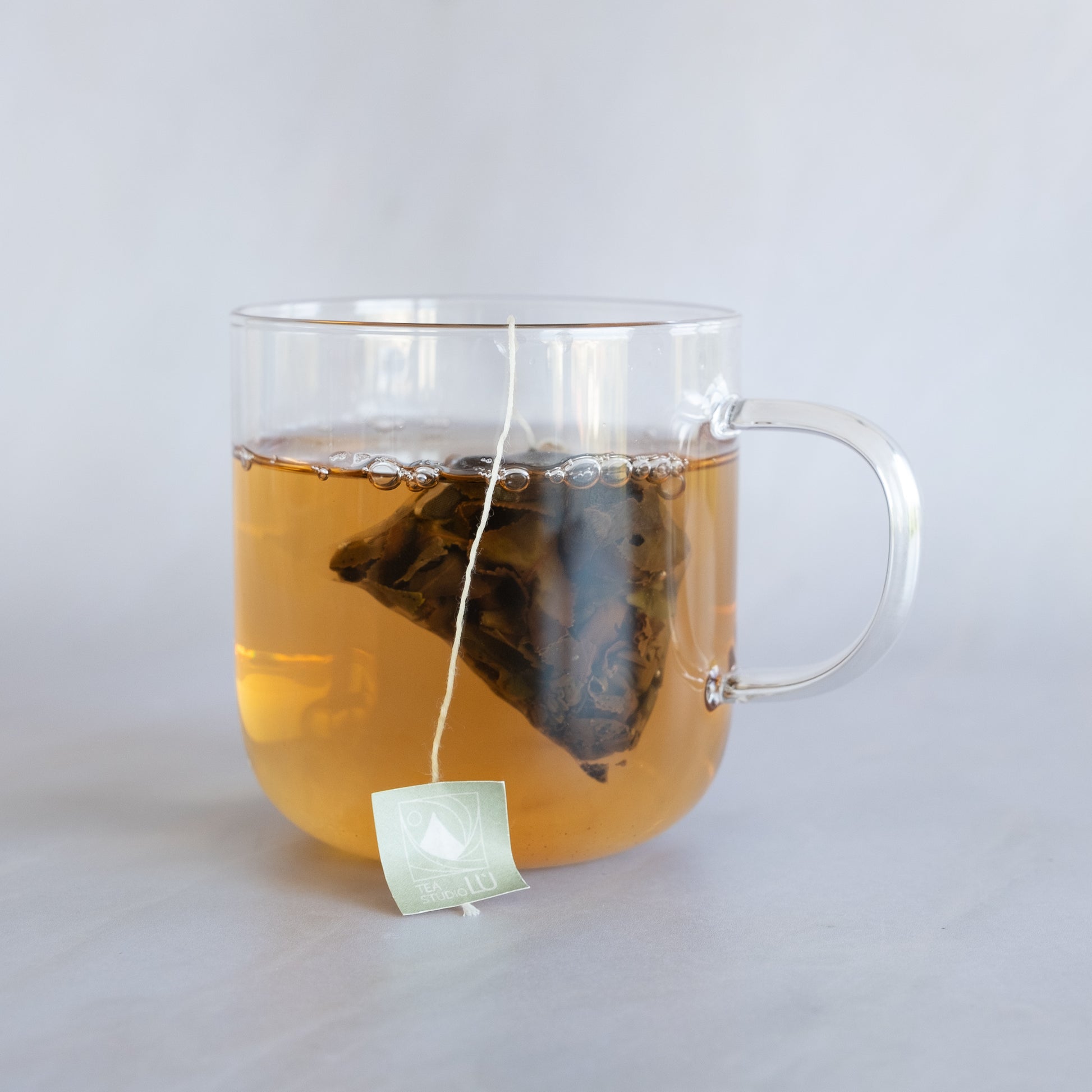 Tea Studio Lu oolong tea sachet steeping in a clear glass mug on a neutral tabletop in Geneva, Switzerland 
