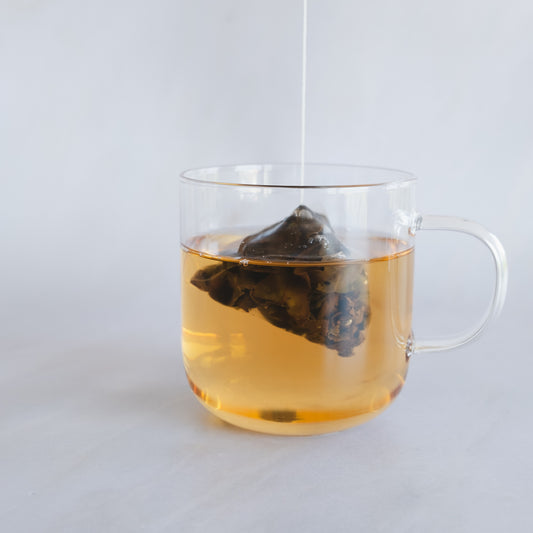 Hand-packed pyramid tea bag lifted above a mug of freshly brewed oolong tea from Tea Studio Lu in Geneva, Switzerland 