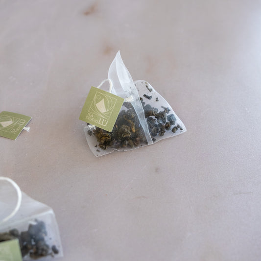 Loose-leaf oolong tea leaves next to a fine-mesh pyramid tea sachet by Tea Studio Lu in Switzerland 